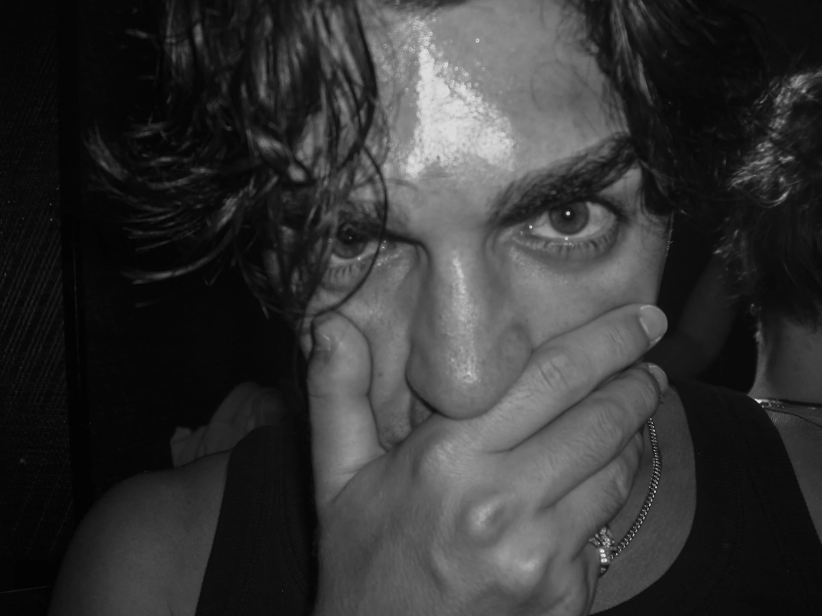 Black and white close-up: a face half covered by a hand, eyes looking straight into the lens.